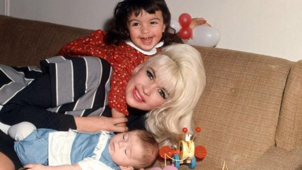 Jayne Mansfield with big blonde hair lays on a sofa with a small baby and young child.
