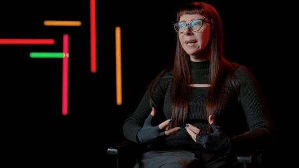 A woman in all black with long straight hair and cat-eye glasses sits discussing movies.
