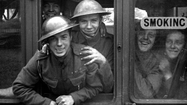 Soldiers in uniform hang out of the open window of a train.