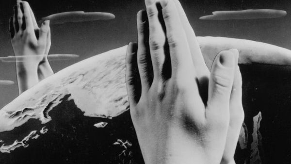 Two large sets of hands in the praying position hover over a black and white earth.