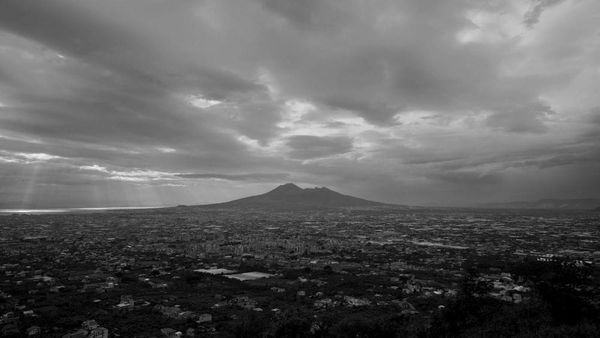 Mount Vesuvius stands tall underneath grey clouds, towering over the city below.