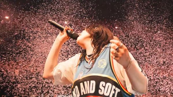 Billie Eilish performs on stage wearing a basketball jersey that reads "Hard and Soft" while confetti falls around her.