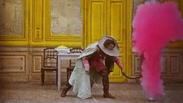 A hand-painted film still of a black and white silent movie. A man in boots, a cape and hat stands in a yellow room as pink smoke envelops him.