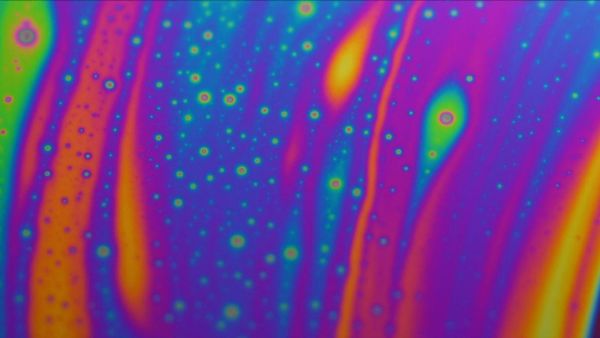 A slick oil effect as purple, orange and green colours clash under a microscope.
