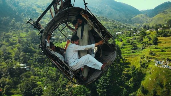 A cable car hangs on an angle over a valley with teenage boys inside holding on.