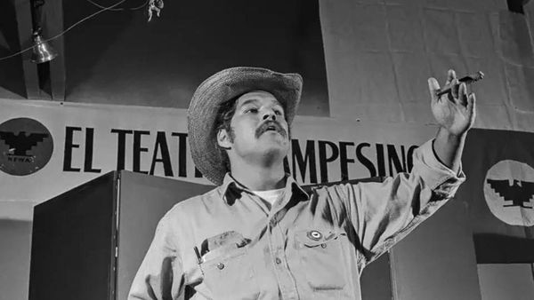 Archival black-and-white image of Luiz Valdez on stage at a theatre holding a cigar.