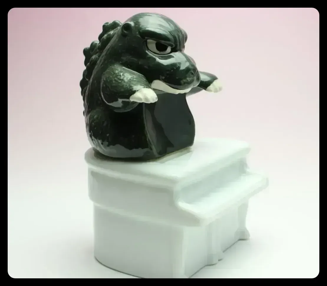 A white ceramic piano with a green Godzilla perched on top.