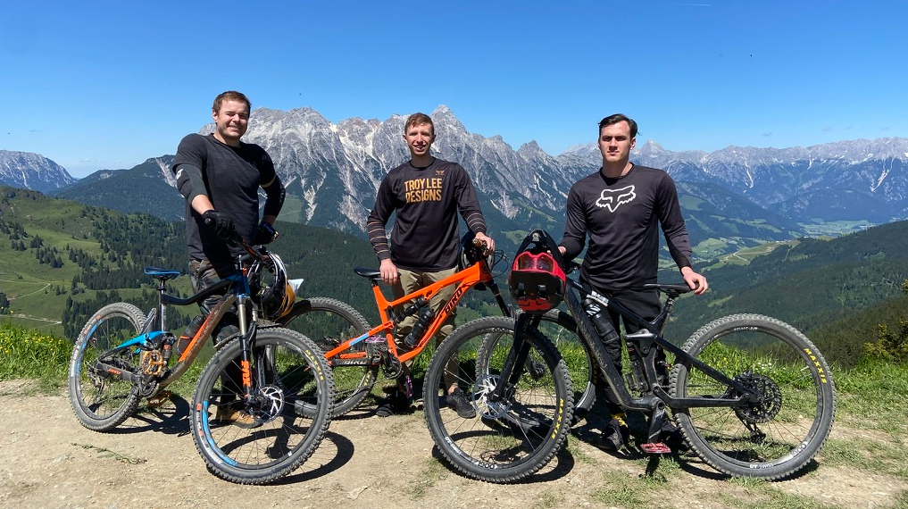 3 people standing behind their bikes with mountains in the backgound