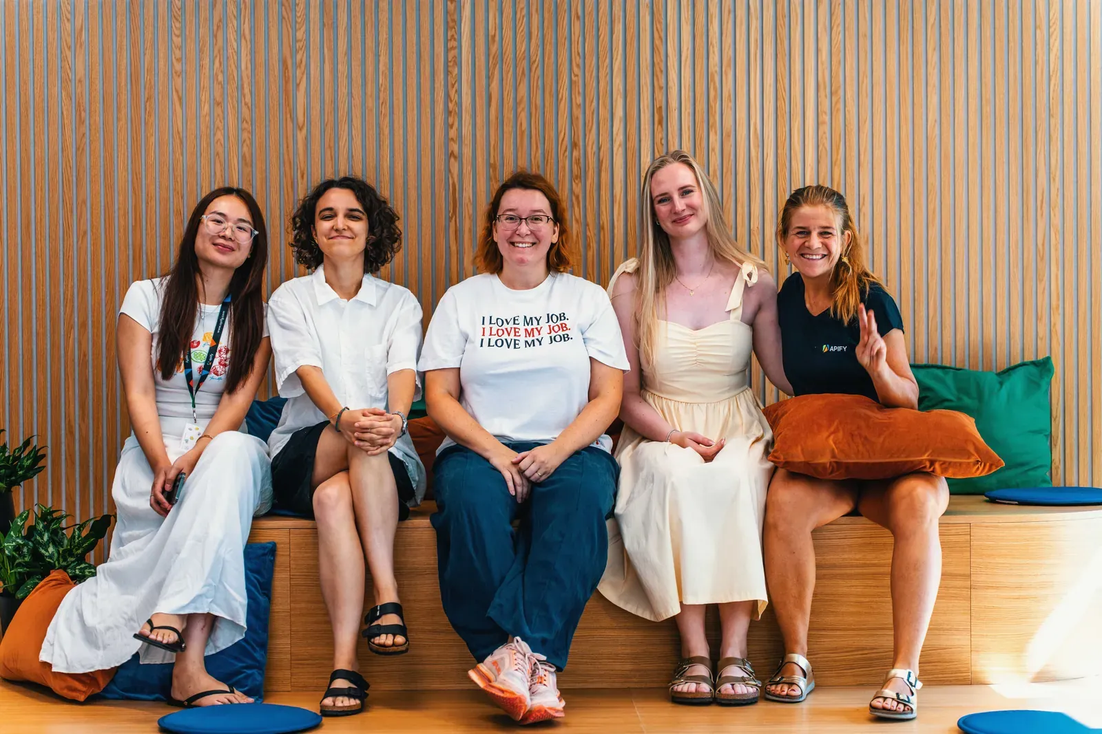 Five members of the Apify Office and Event team sitting together on a wooden bench in the new office