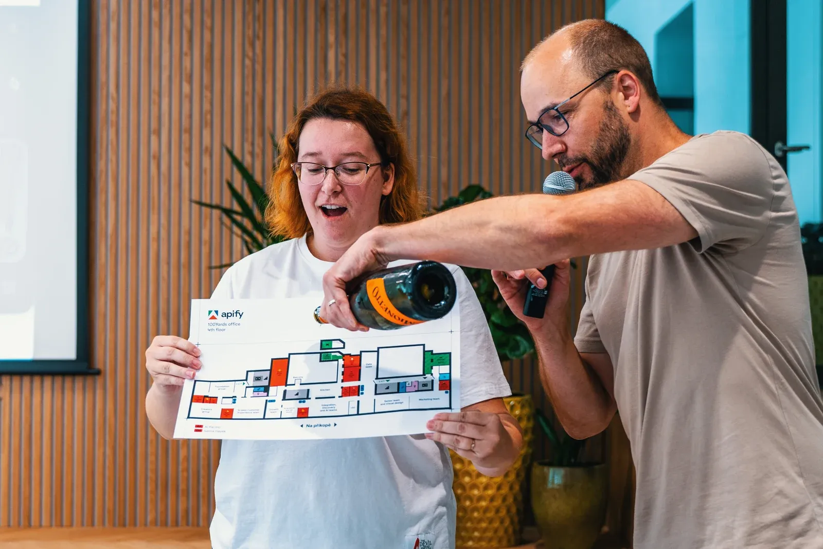 Martina Bovanova holds up a printed floor plan of the new Apify office while Jan Curn pours champagne over it