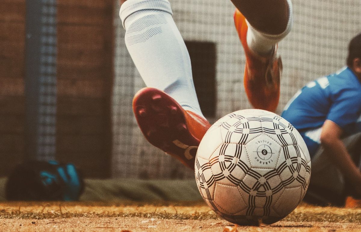 Feet in football gear kicking a football on a field.