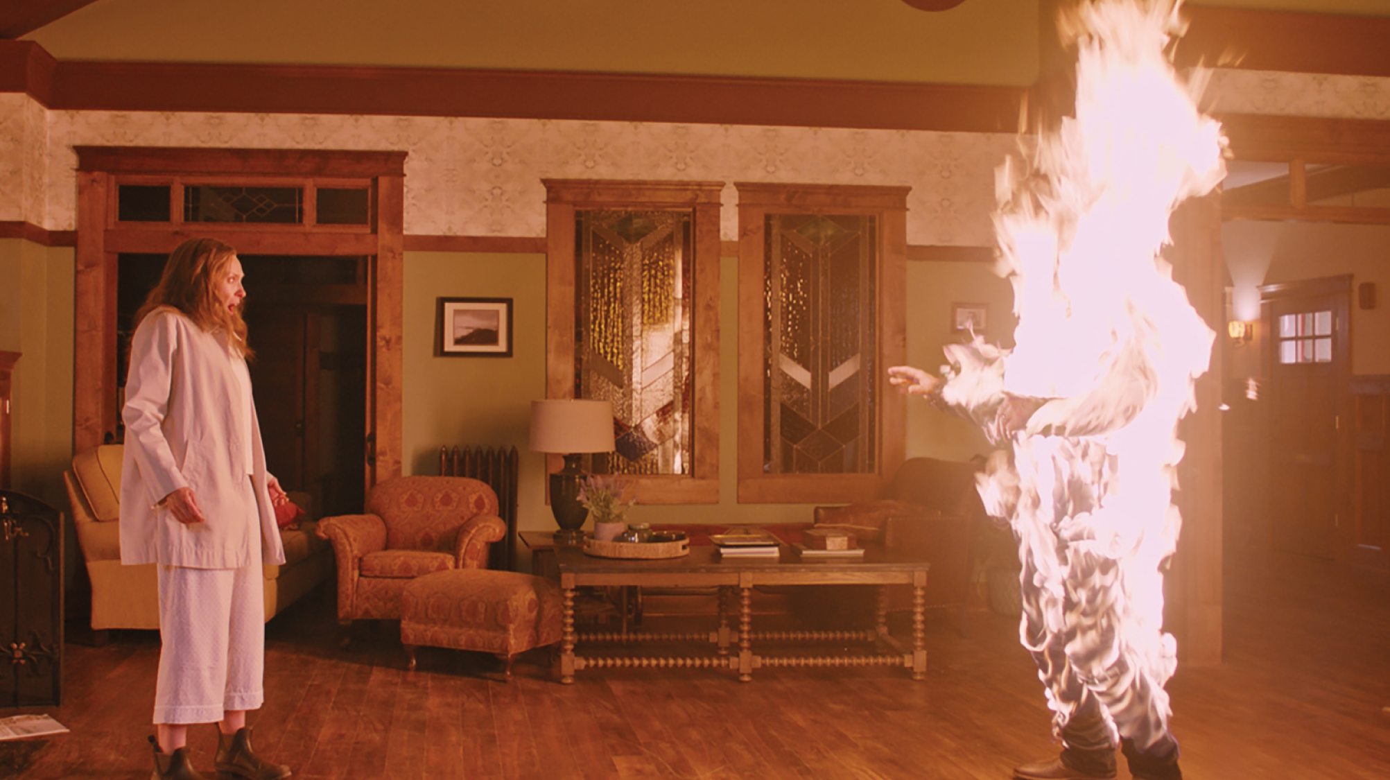 A still from the film Hereditary showing a woman looking shocked at someone set on fire in front of them.