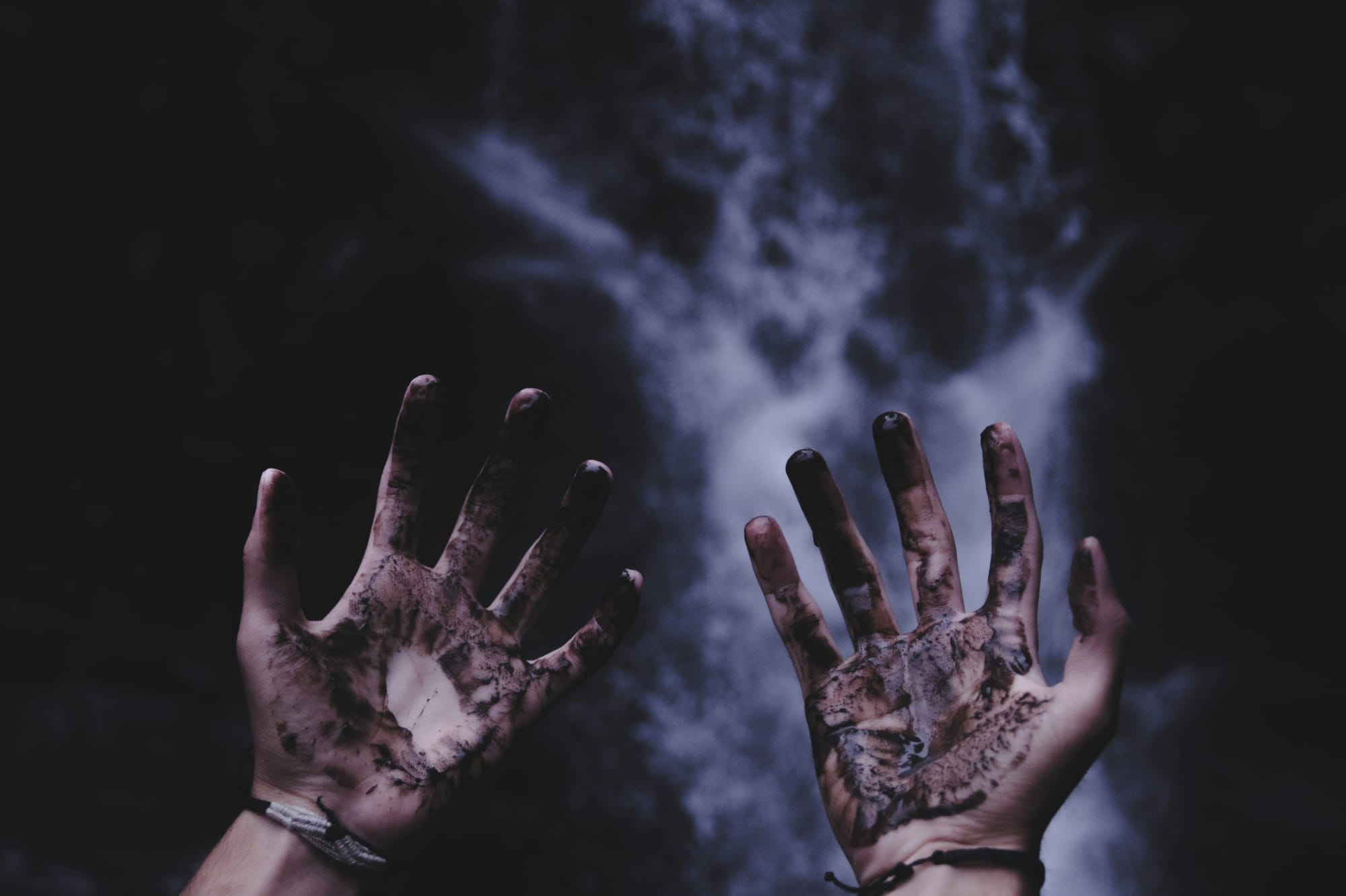 A photo of a pair of hands covered in black ash, with a smoke cloud in the background.