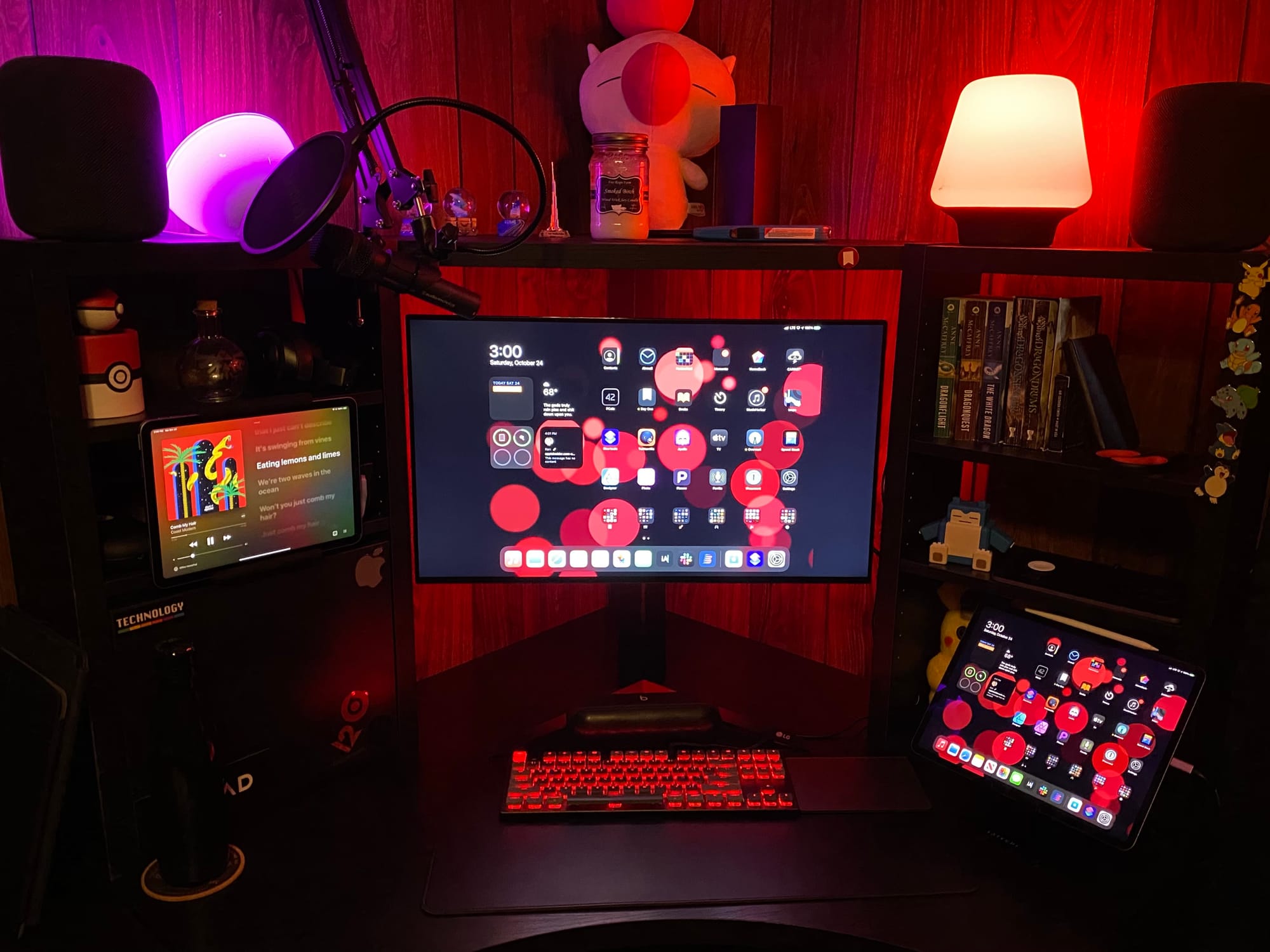 An iPad Pro connected to a monitor, an iPad Air on the side, on a black desk with assorted nerd culture goods cast in a red light.
