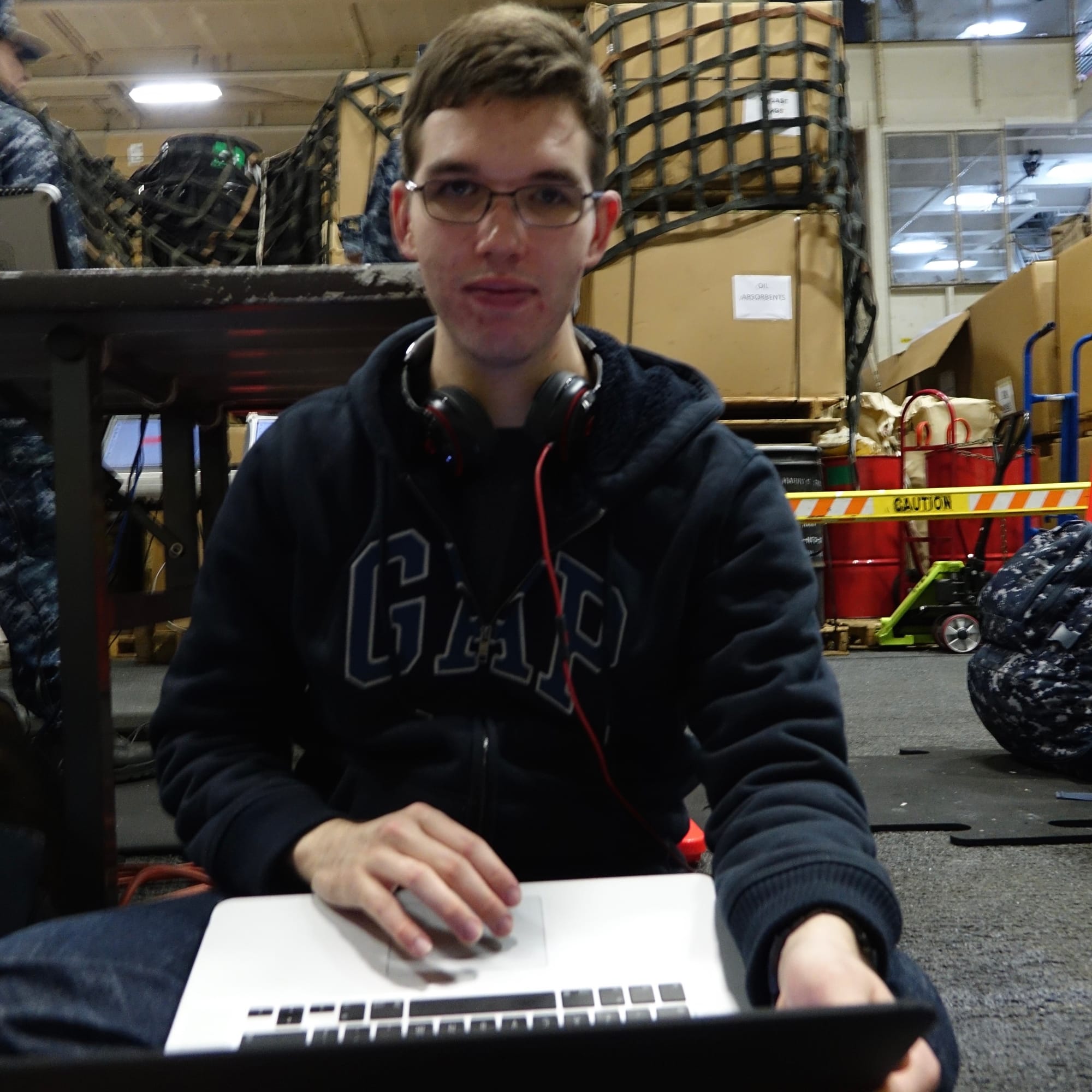 Wesley Hilliard in a GAP hoodie holding a MacBook Pro in an aircraft carrier hanger bay