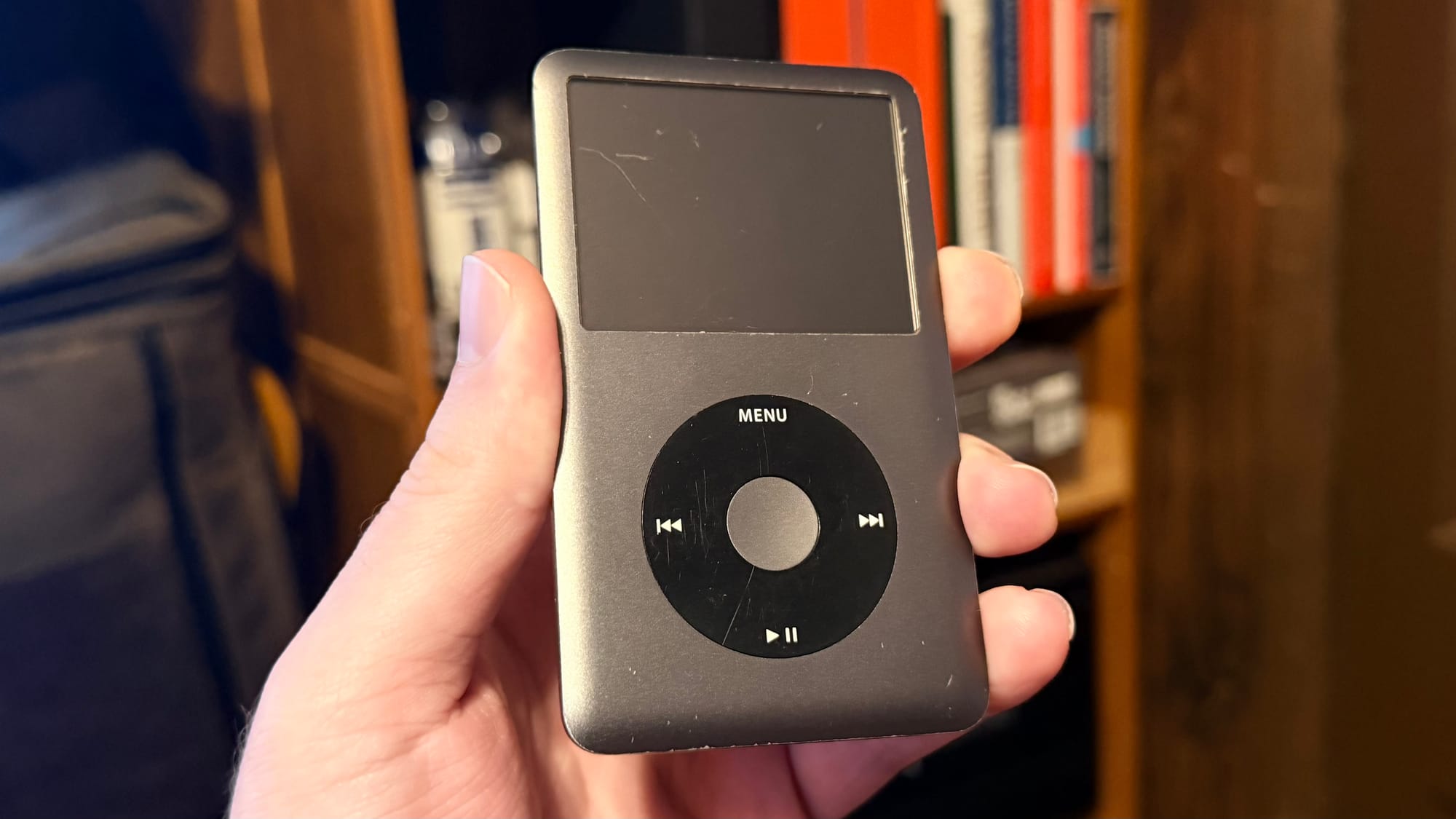 An old scratched up iPod video held in a hand in front of a bookshelf