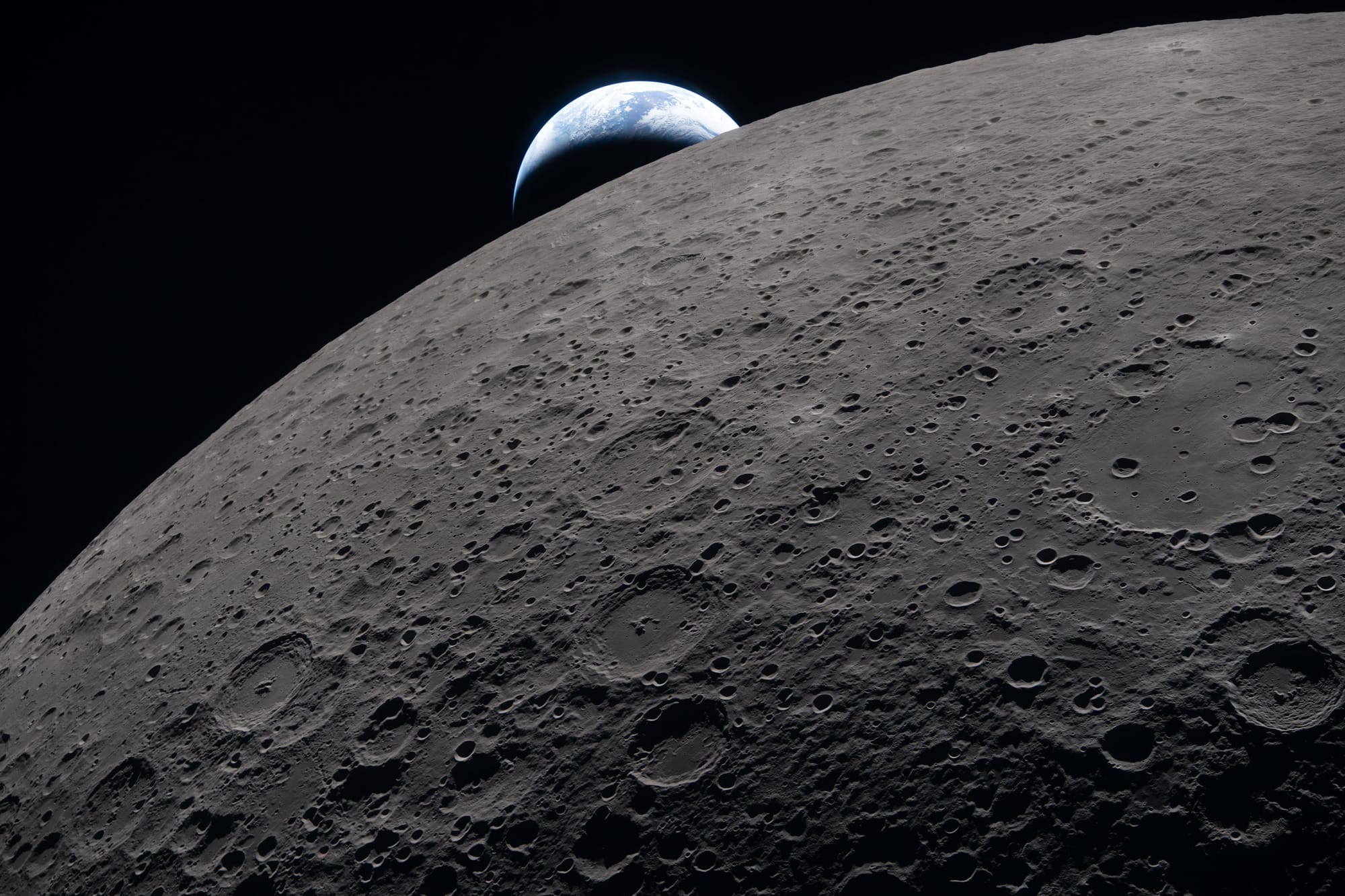 A photo captured from the Artemis crew flying behind the moon, showing the earth viewed peeking over the moon's horizon