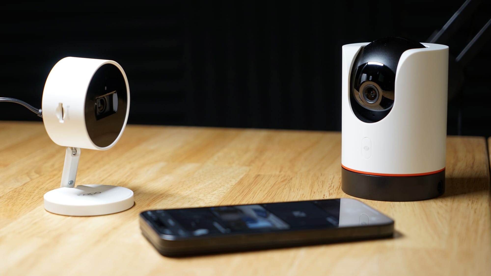 Two security cameras on a table with an iPhone face up between them
