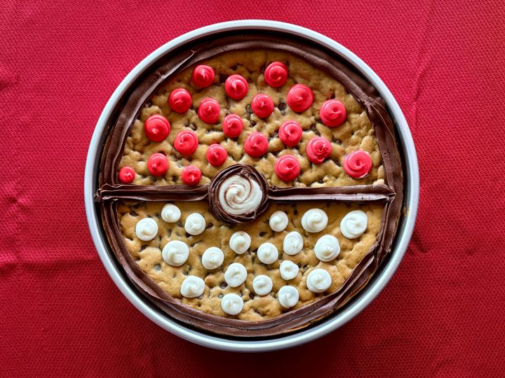 A cookie cake with red and white icing in the shape of a pokeball from Pokemon