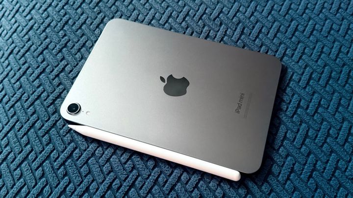 An iPad mini 7 with Apple Pencil Pro laying on blue patterned fabric.