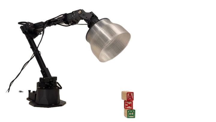 A lamp on a robotic arm stands over a few blocks with the letters AYB stacked.