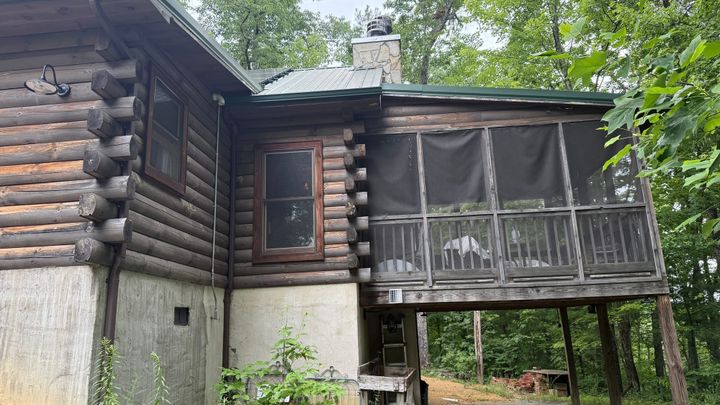 A photo of a cabin with a screened in porch above a small car port.