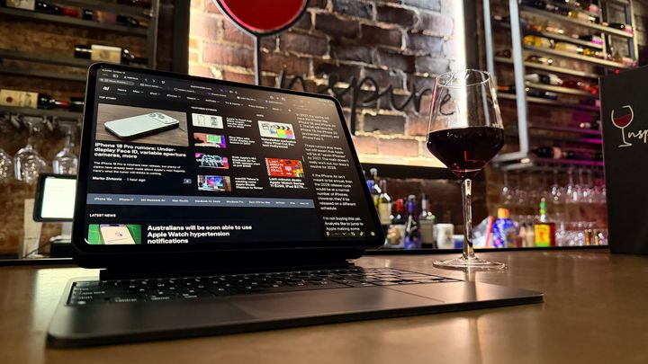 An iPad Pro in a Magic Keyboard next to a glass of wine with an Inspire Wine logo in the background