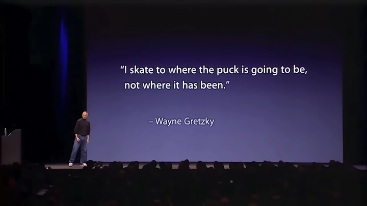 Steve Jobs on stage during the iPhone reveal event, the slide reads 'I skate to where the puck is going to be, not where it has been. - Wayne Gretzky'