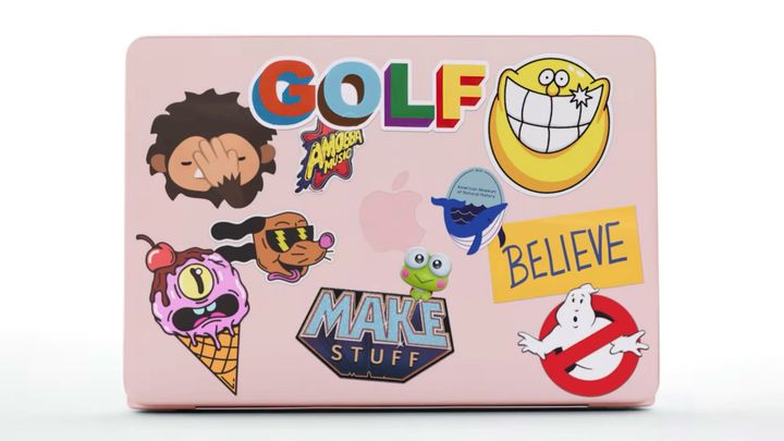 A blush MacBook Neo covered in stickers featuring Ghostbusters, Ted Lasso, Tamagotchi, and Sneaky Sasquatch