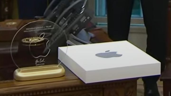 The glass and gold plaque with an Apple logo and Cook's signature on Trump's desk by a white box with a gray Apple logo