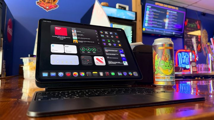 An iPad Pro in the Magic Keyboard by a beer can featuring a frog wearing a crown, sitting on a bar top