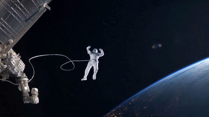 An astronaut tethered to a spacecraft taking a selfie with an iPhone above Earth