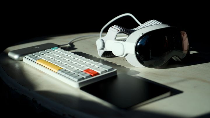 Apple Vision Pro on a dramatically lit table by a Magic Trackpad, Nuphy keyboard, and battery