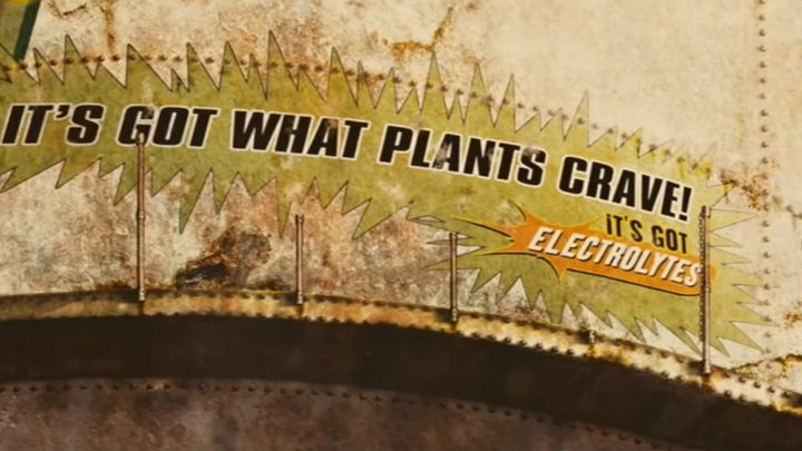 A scene from "Idiocracy" showing a water tower with the Brawndo catchphrase "It's got what plants crave! It's got electrolytes."