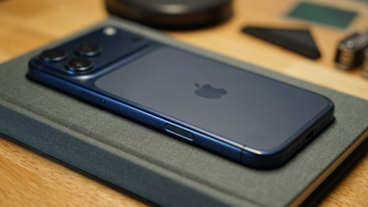 A blue iPhone 17 Pro Max laying on a gray notebook on a desk