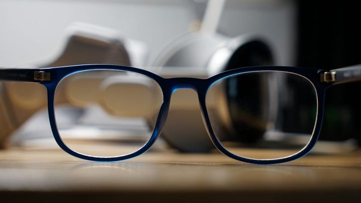 A pair of blue glasses with an Apple Vision Pro blurred behind the lenses