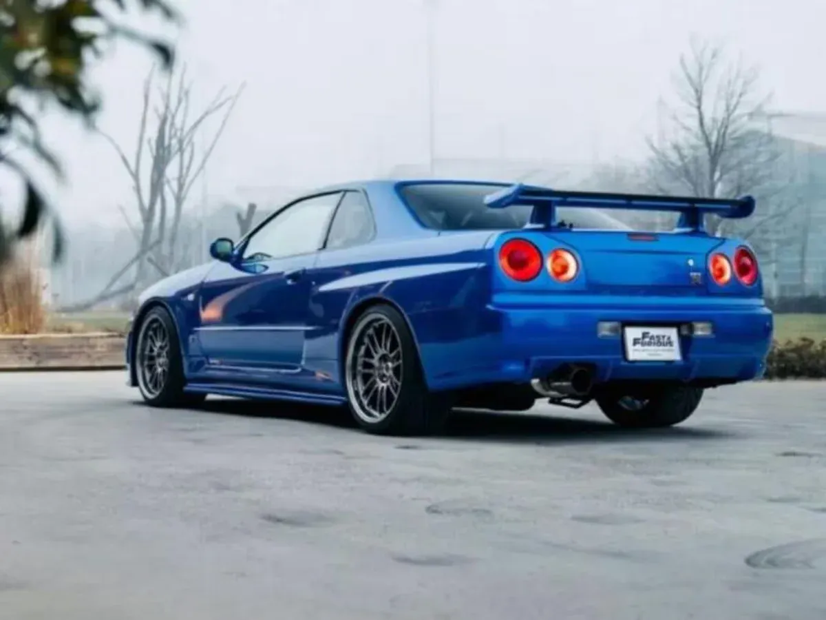 Vista trasera de un Nissan Skyline GTR R34 en color Bayside Blue, mostrando sus icónicas luces traseras redondas y su alerón trasero.