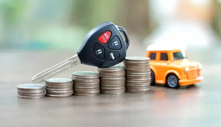Llave de auto sobre pilas monedas y al lado un naranja