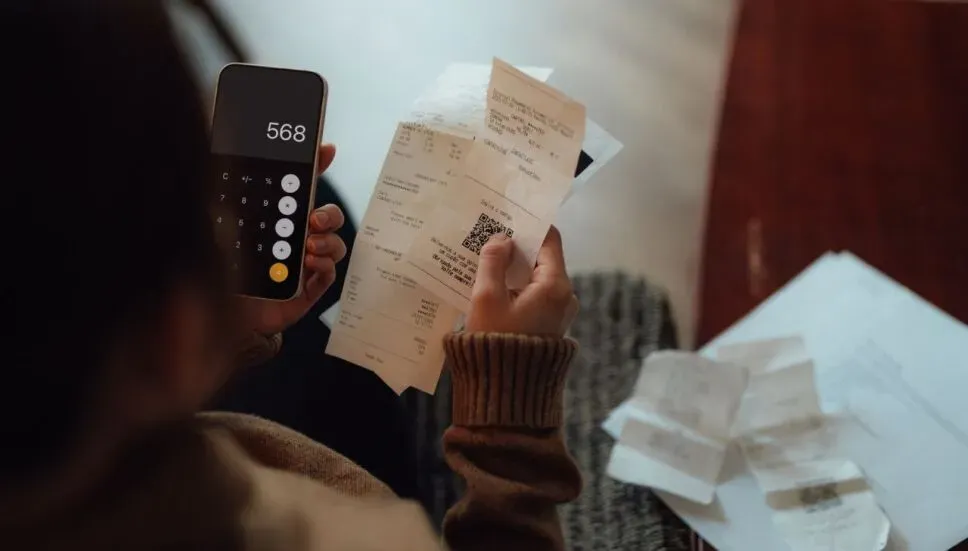 Persona con recibos en una mano y un teléfono móvil en otra usando la calculadora para organizar gastos deducibles.