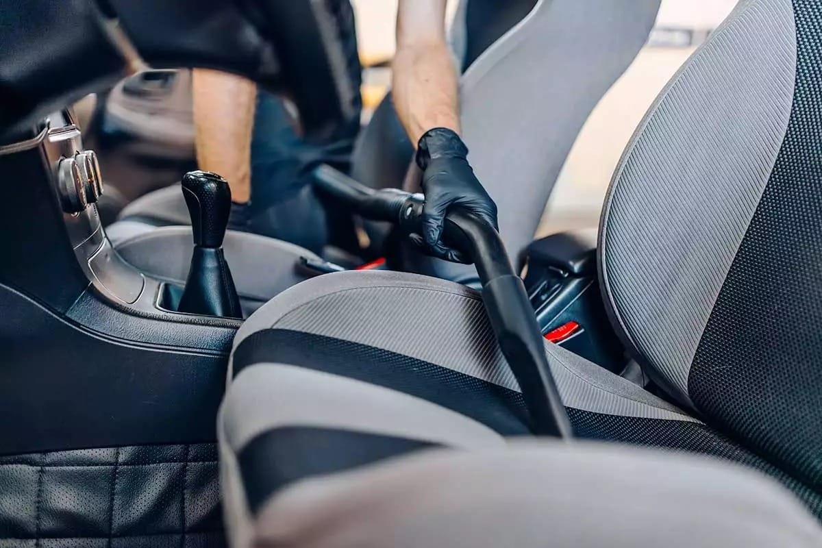 Mano sosteniendo aspiradora sobre asiento de auto
