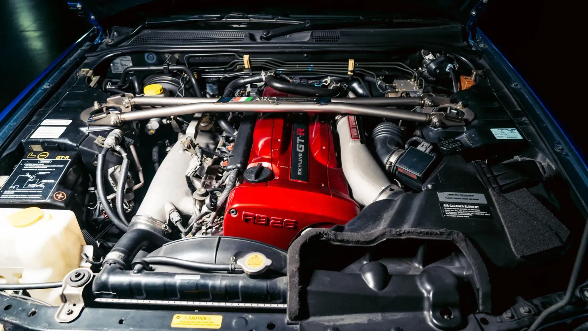 Primer plano del motor RB26DETT de un Nissan Skyline GTR R34, destacando su doble turbocompresor y la icónica cubierta de válvulas.