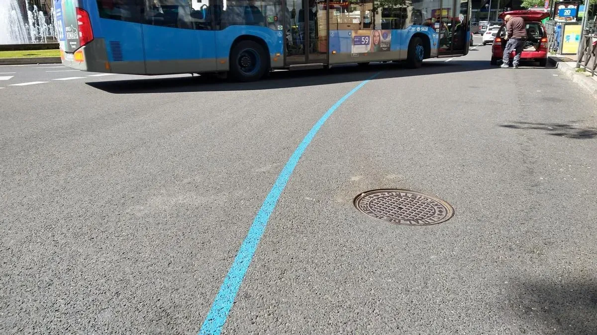 Detalle de una línea azul pintada sobre el asfalto junto a la banqueta