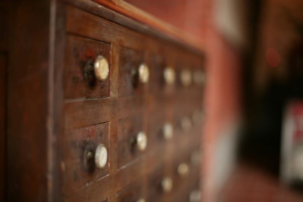 Rows of small drawers in an old worn wooden cabinet with pale round knobs and faint hand-marked labels, receding into soft focus.