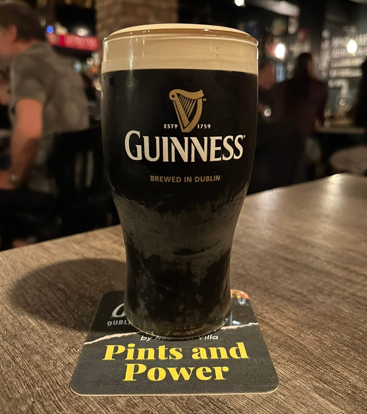 A perfectly poured Guinness, foam dome perfectly atop. The glass, classic tulip glass sits on the table atop a beermat that reads "Pints and Power"