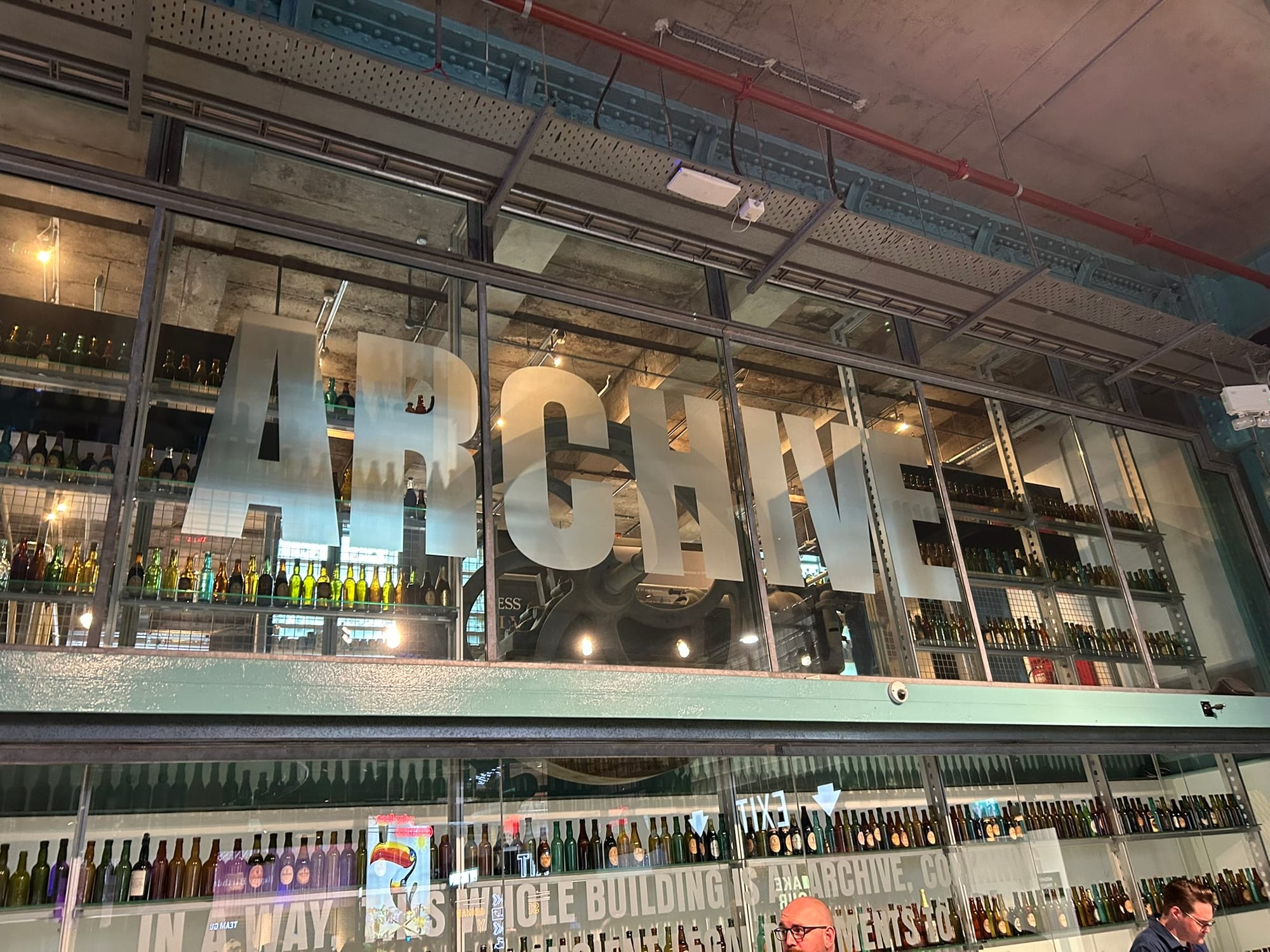 A second floor above the tour hall with the word "ARCHIVE" etched across the full glass wall.
