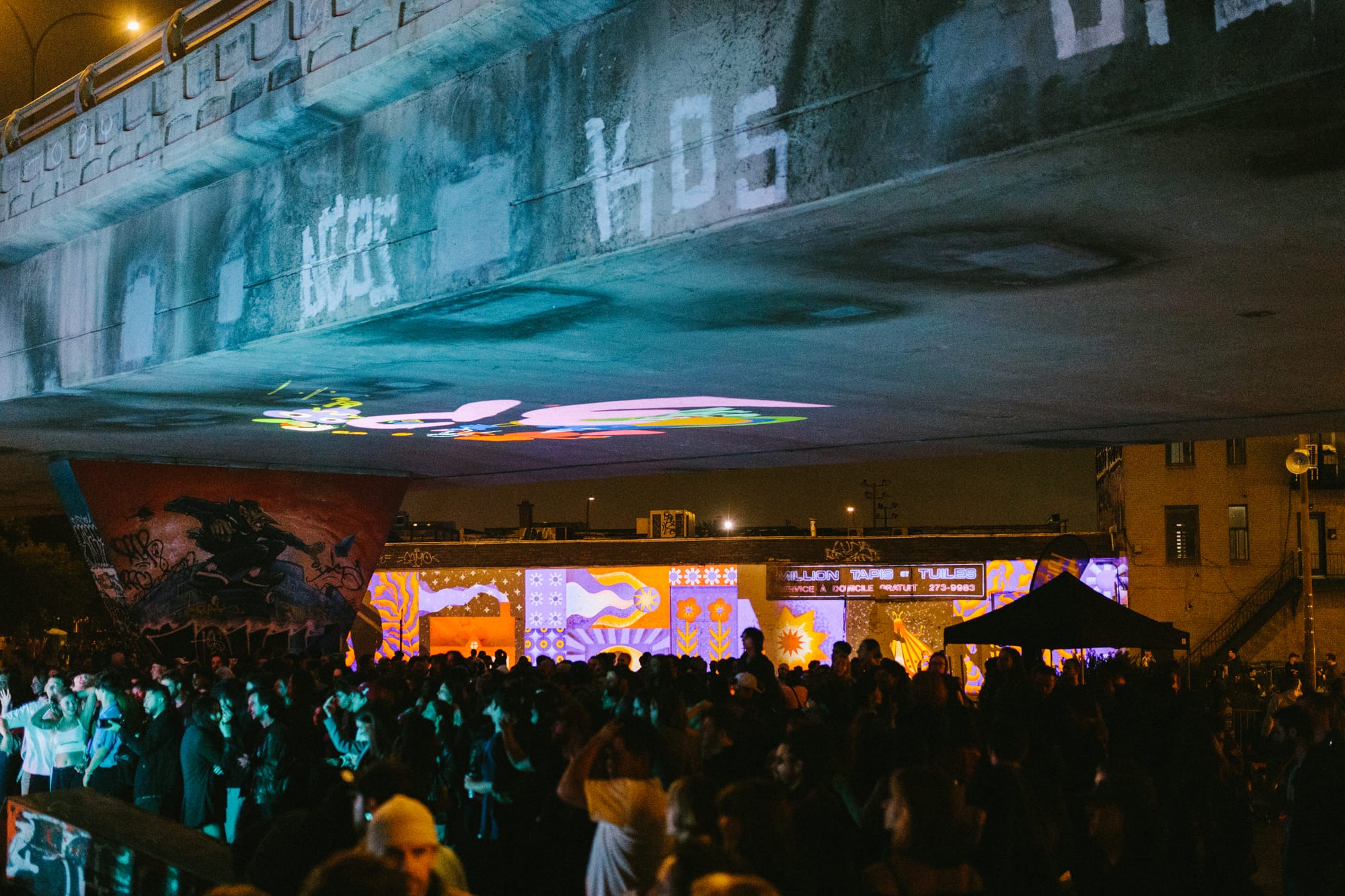 Des festivaliers sous le viaduc Van Horne-Rosemont, alors que des images sont projetées sur des structures environnantes.