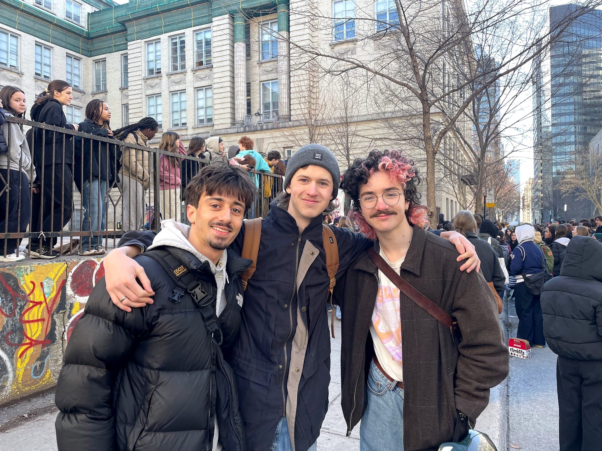 Les trois élèves posent sur le trottoir devant la cour d'école et les autres manifestants.