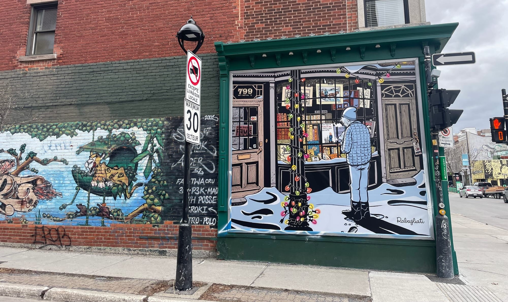 La photo montre le mur extérieur de la Bouquinerie du Plateau où se trouve la murale avec le personnage de Paul en hiver.