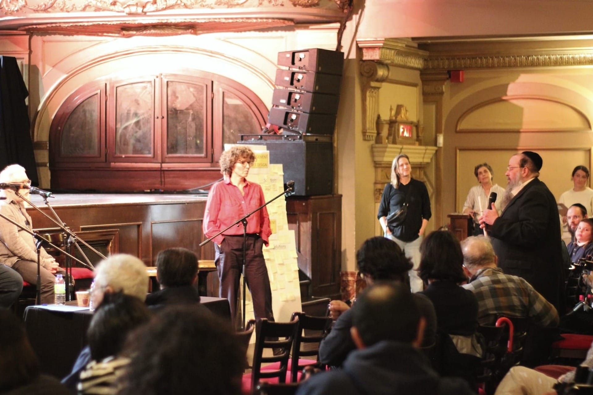 M. Feig debout parmi le public, microphone à la main, s'adressant aux panélistes.