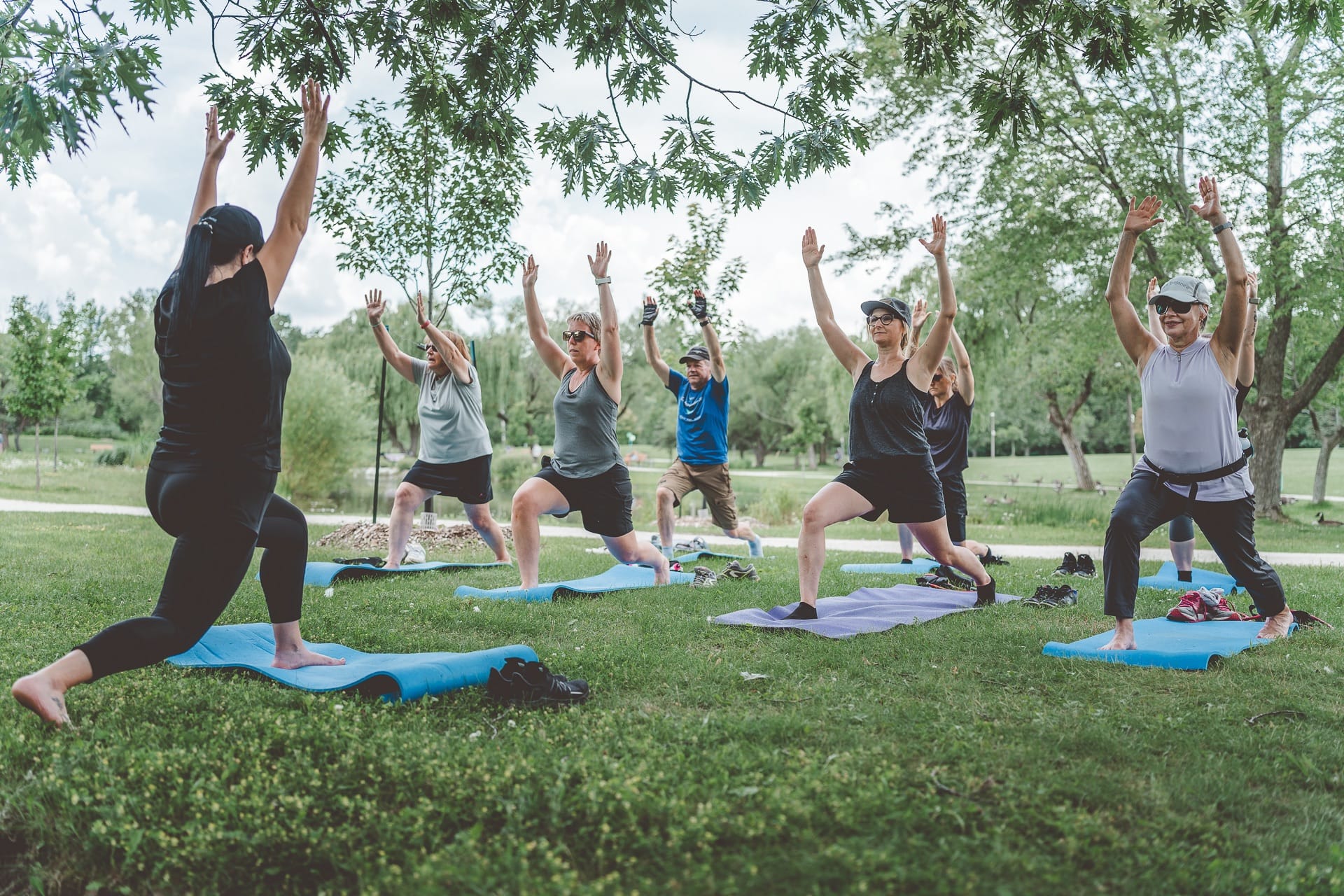 Huit adultes font des étirements sur un tapis de sol dans un parc en été.